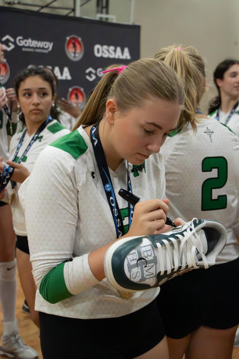 Senior Janna Boren signs junior Arielle Yapi's dad's shoe after the state championship win.