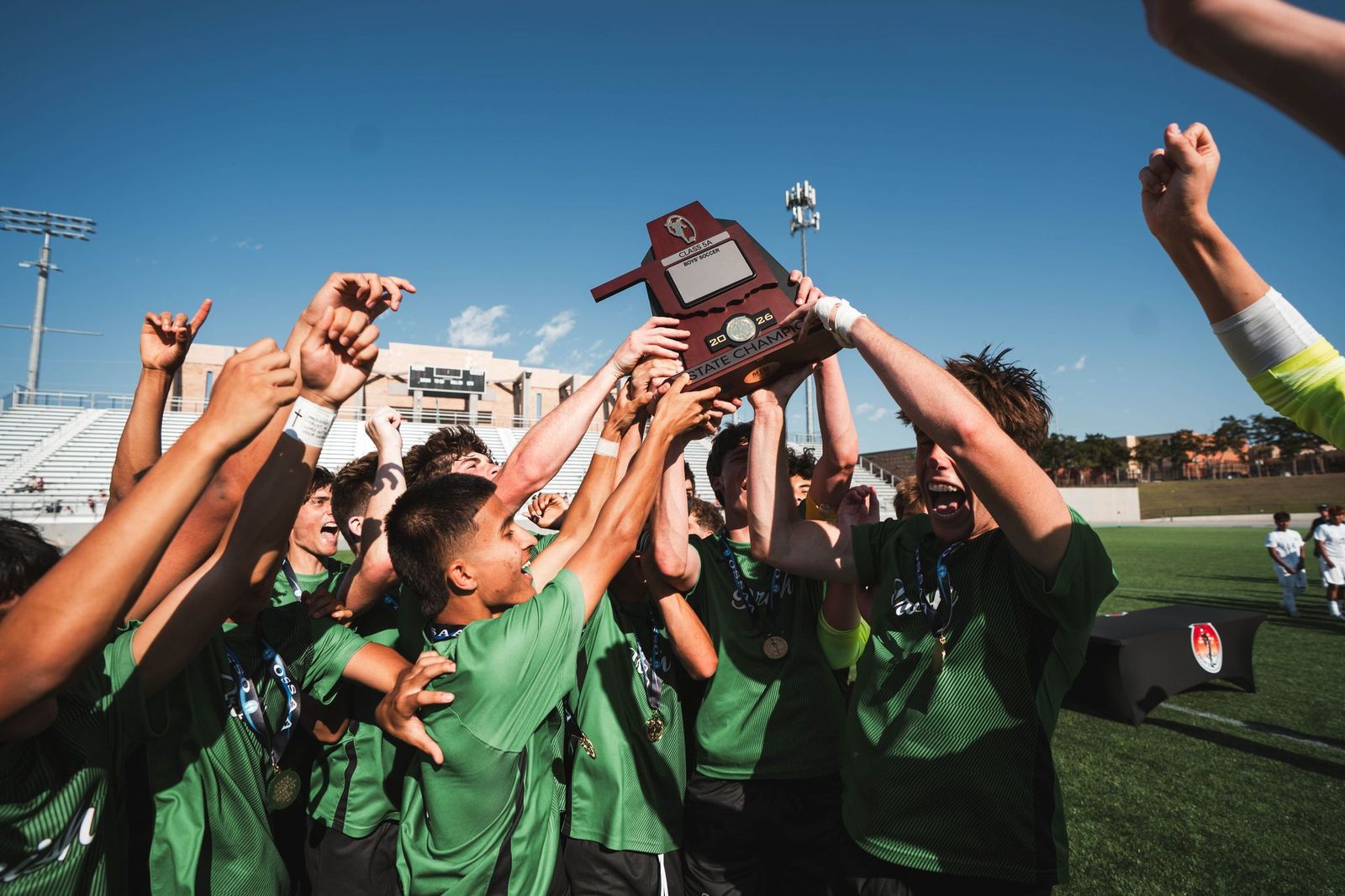 The Boys Soccer team cheers with their State Championship trophy.